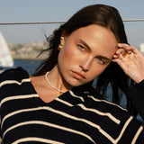 Woman wearing a black and white striped sweater with a scenic background wearing petite pearl necklace and vintage inspired gold earrings