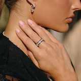 A close-up lifestyle shot of a woman wearing a diamond band ring on her finger, with her hand resting on her neck. She is wearing a silver-toned dangle earring and a delicate silver necklace, dressed in a black lace top.
