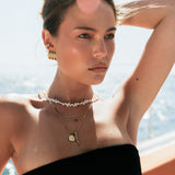 Woman wearing gold jewelry and a black strapless top with a blurred background