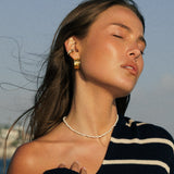 Woman in a black and white striped sweater and white bikini sitting on a boat with water and sky in the background. wearing waterproof jewelry and pearl choker